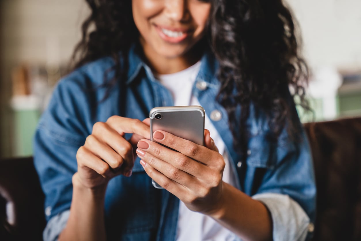 Cropped shot of an african-american young woman using smart phone at home. Smiling african american woman using smartphone at home, messaging or browsing social networks while relaxing on couch Man Performing Google Search for Colorado Personal Injury Lawyers